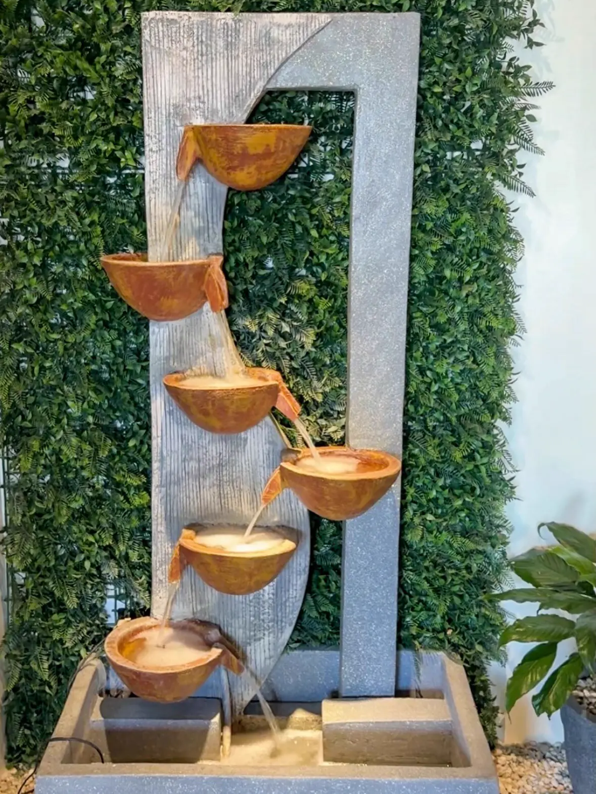 Tiered water fountain against a green wall